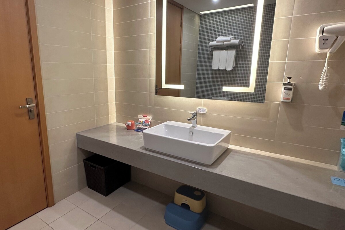 Une salle de bain moderne avec un grand miroir, un lavabo et un sèche-cheveux fixé au mur.