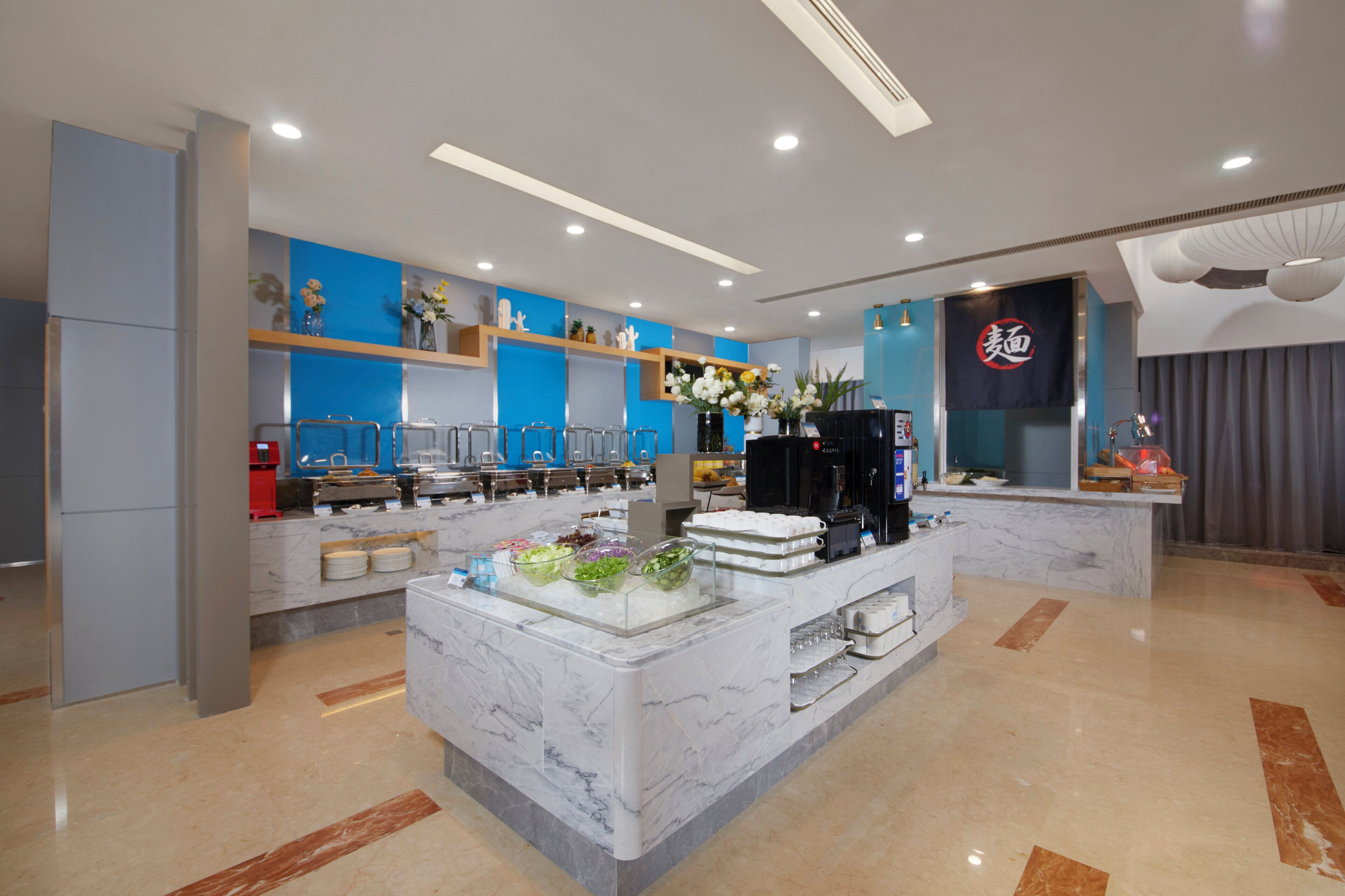 Un hall d’hôtel moderne avec un comptoir d’accueil en marbre, un espace buffet proposant divers plats et un grand écran numérique affichant un logo.