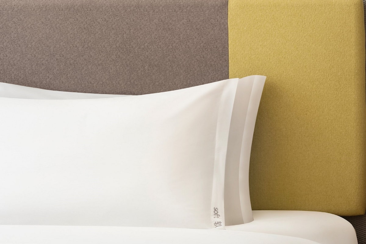 Ein Bett mit weißer Bettwäsche und einem Kopfkissen mit sichtbarem Markenlogo.