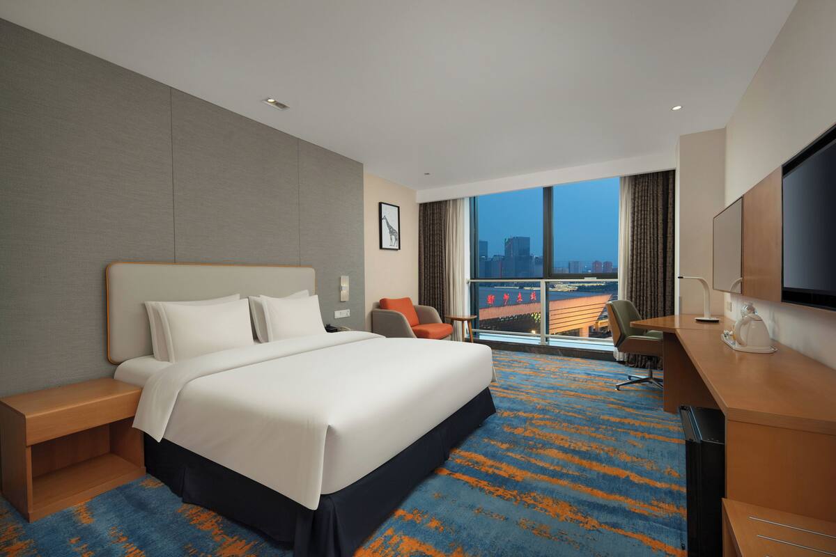 Ein Hotelzimmer mit einem großen Bett, einem Schreibtisch, einem Sessel und einem Fernseher.