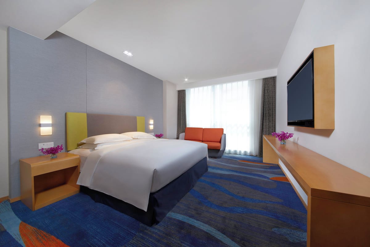 A modern hotel room with a large bed, a flat-screen TV, a desk, and a comfortable seating area.