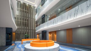 Un hall d’entrée moderne doté d’un espace salon circulaire, d’un plafond haut avec des luminaires encastrés et d’un mur en marbre.