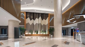 Un hall d’entrée spacieux au design moderne, agrémenté de grandes colonnes, d’un comptoir de réception et de plantes en pot.