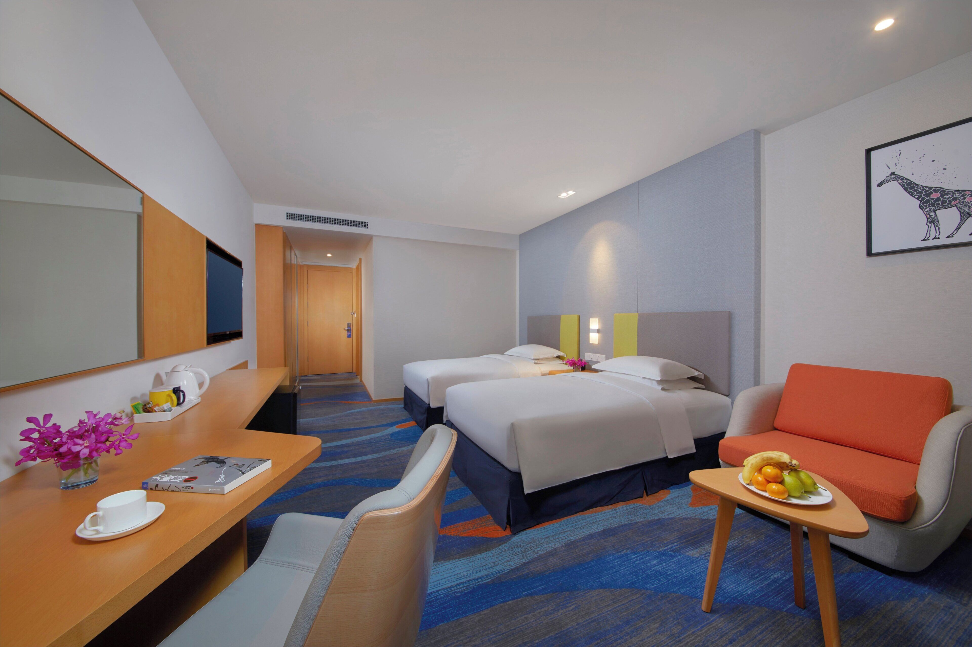 Une chambre d’hôtel avec un lit, un bureau et une chaise, un canapé et une petite table avec des fruits.