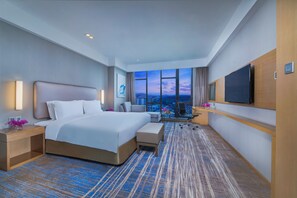A hotel room with a large bed, a desk, a chair, a TV, and a view of the cityscape. - Holiday Inn Express Guian Yungu by IHG (Anshun)