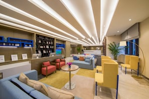 Un moderno vestíbulo de hotel con una recepción, zona de estar y una pantalla grande mostrando un evento deportivo.