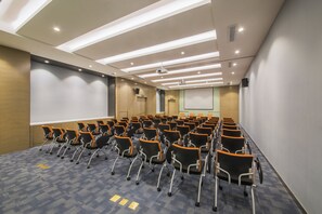 A conference room with rows of chairs, a projector screen, and a presentation screen.