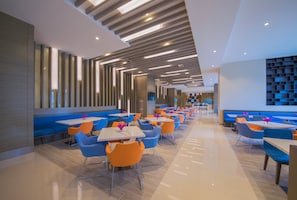 Un restaurante moderno con una barra alargada, asientos en azul y naranja y un diseño de techo contemporáneo.