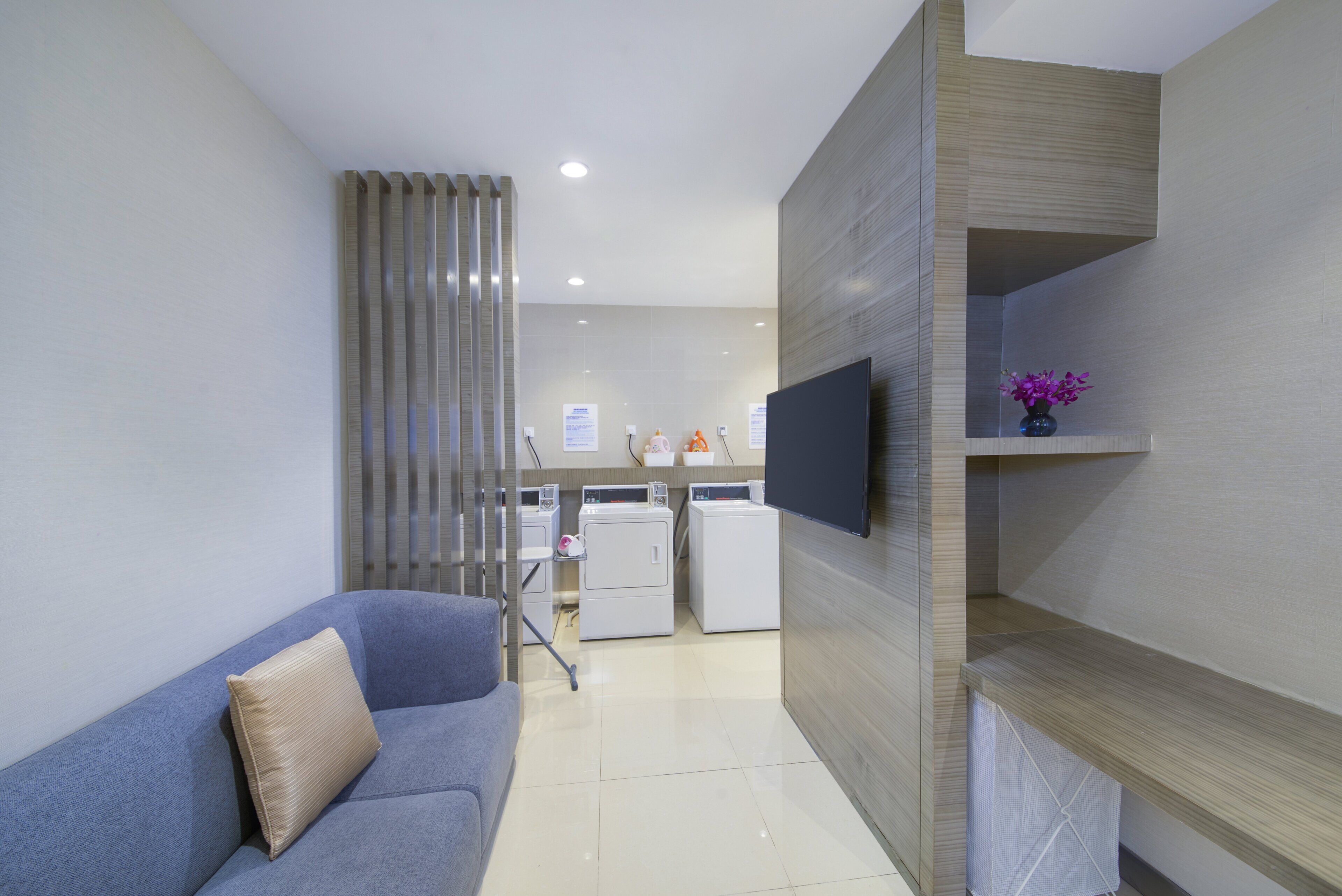 Una sala de estar moderna con un sofá gris, un televisor de pantalla plana montado en la pared y un estante con un florero.