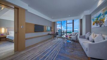 A modern hotel room with a large window, a flat-screen TV, a sofa, a coffee table, and a painting on the wall.