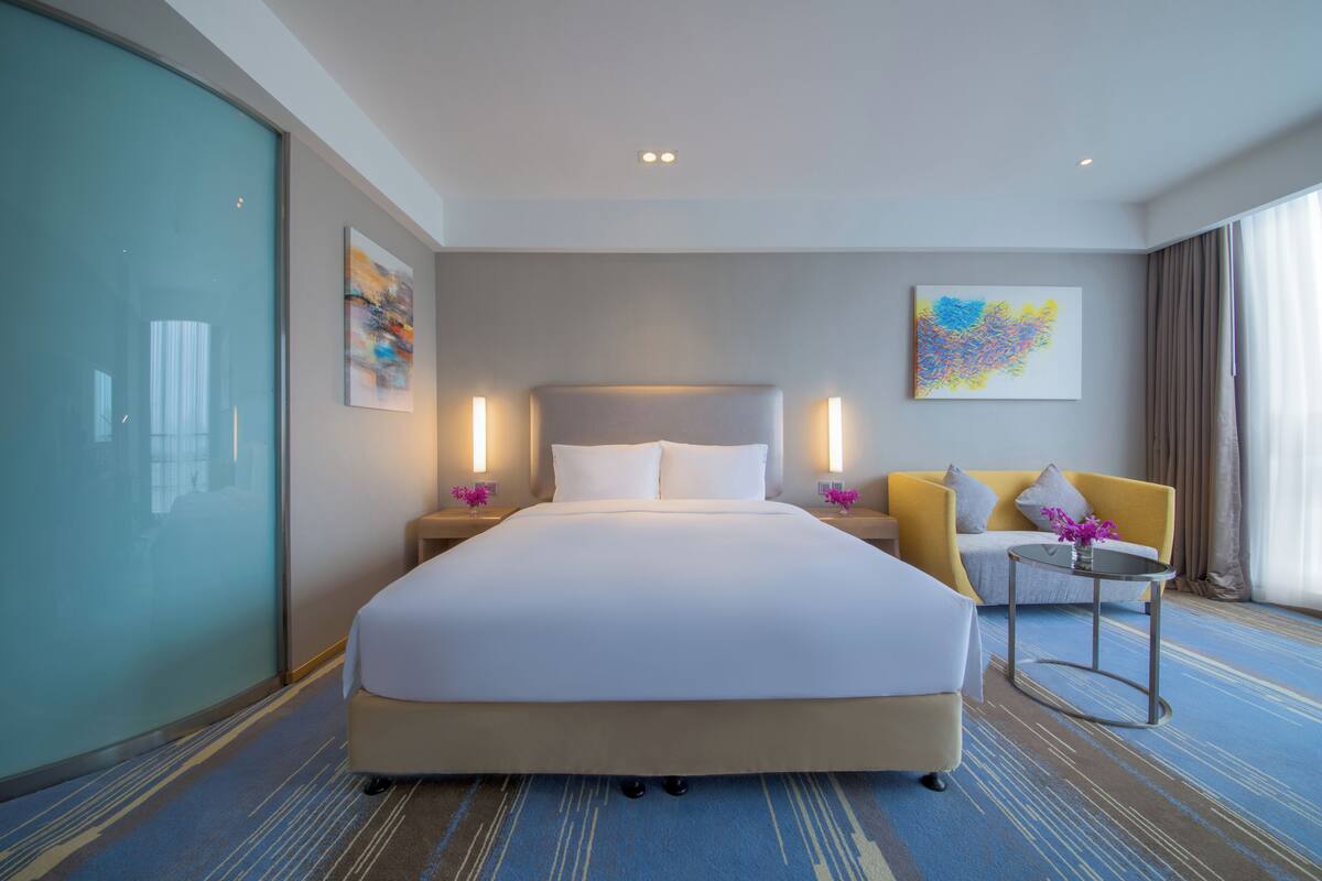 Ett modernt hotellrum med en stor säng, en soffa, ett litet bord och en tavla på väggen.