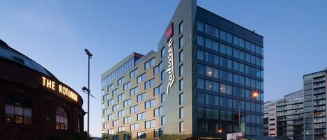 Ett modernt hotell med en framträdande skylt, stora fönster och en väl upplyst entré.