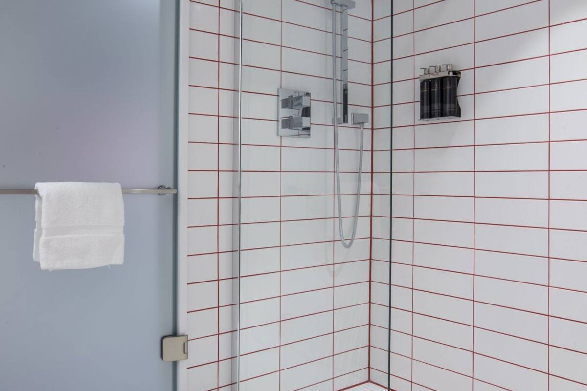 Eine moderne Dusche mit Glastür, einer weiß gefliesten Wand mit roten Linien und einem weißen Handtuch am Türgriff.