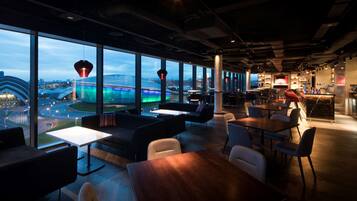 A modern lounge with large windows, seating areas, and a bar.
