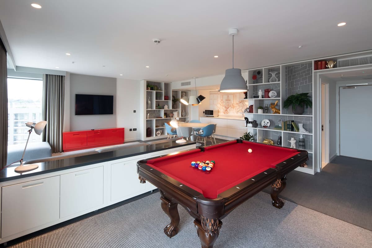 Ein modernes Wohnzimmer mit Billardtisch, einem roten Sofa und einem an der Wand befestigten Fernseher.