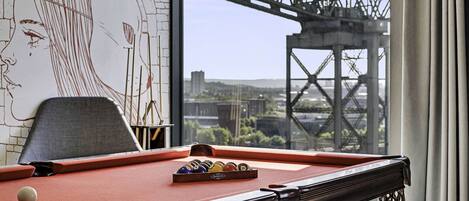 A pool table with a view of a bridge and cityscape through a window.