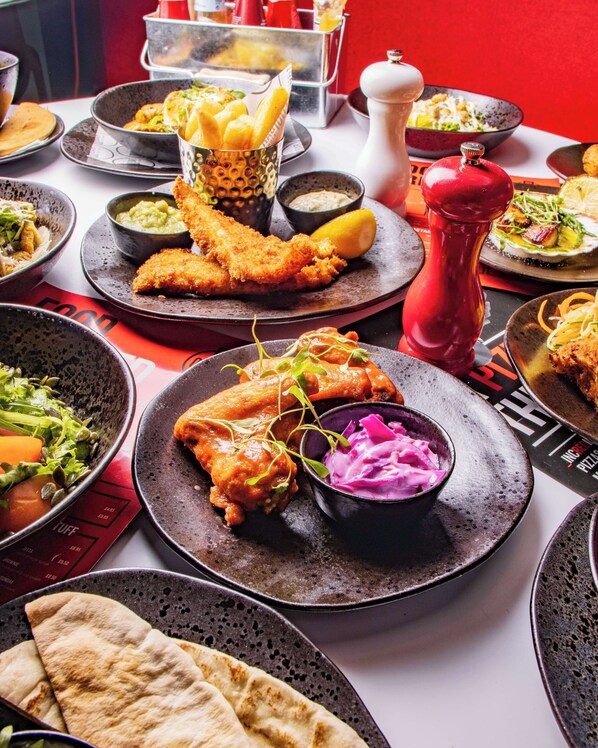 Variedad de platos, incluyendo pescado frito, pan y ensalada, sobre una mesa con fondo rojo.