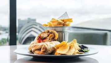 Un plato con un wrap, papas fritas, patatas fritas y una ensalada sobre una mesa con vistas a edificios al fondo.