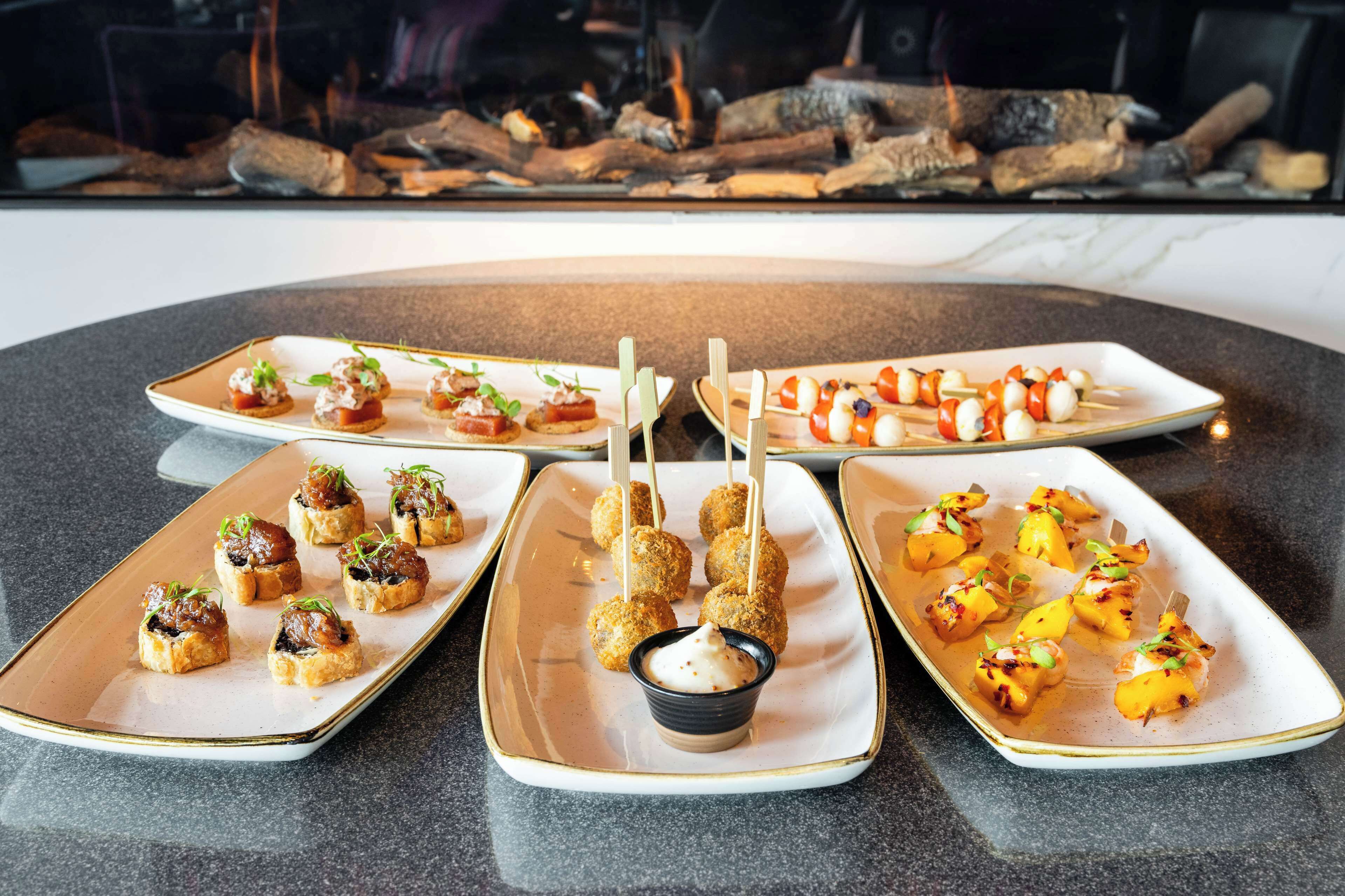 Tres platos rectangulares de aperitivos sobre una mesa con superficie de mármol.