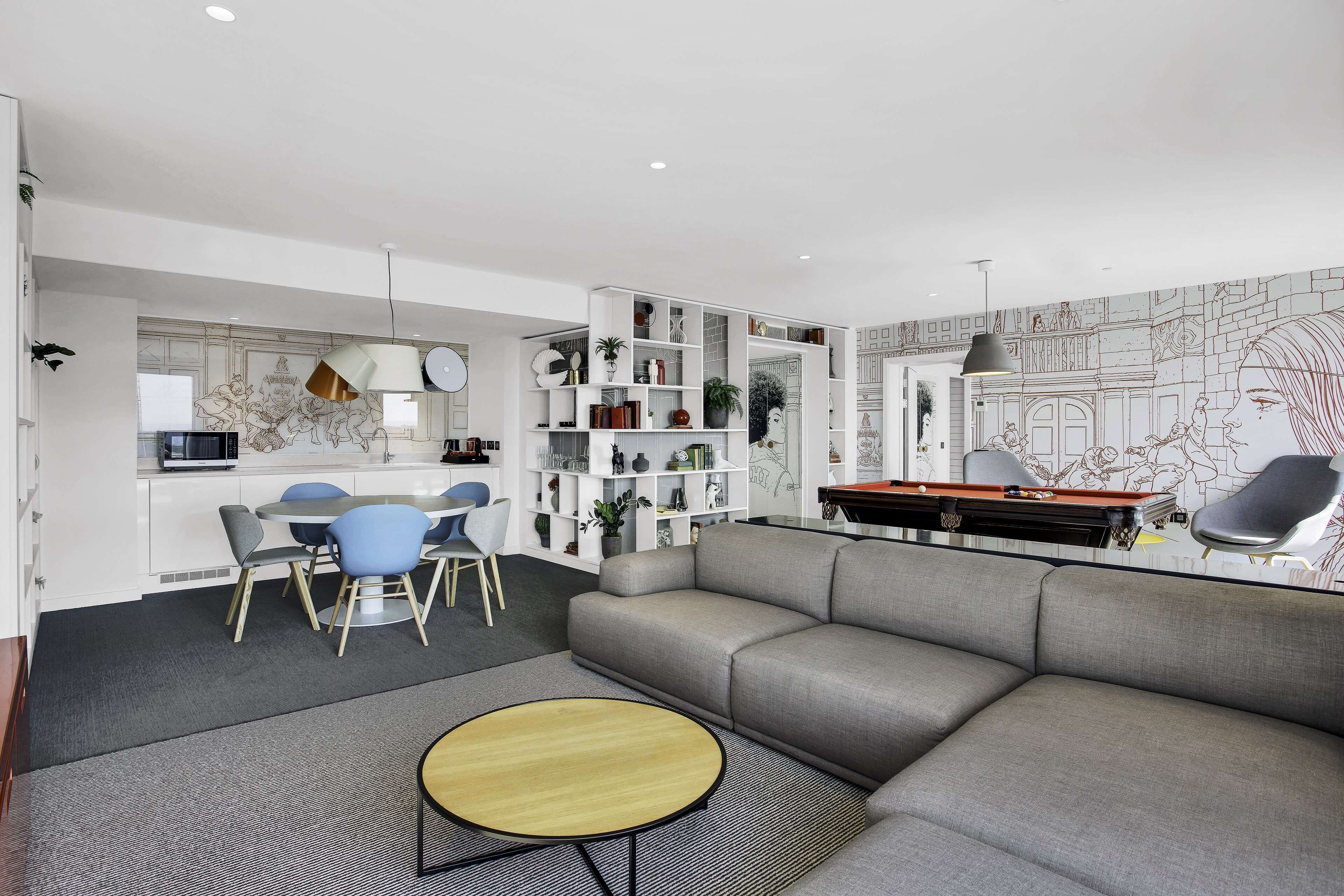 Una sala moderna con un sofá gris, una mesa de centro redonda y una zona de comedor con sillas azules.