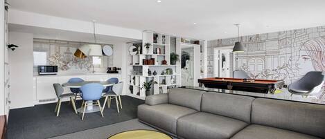 Una sala moderna con un sofá gris, una mesa de centro redonda y una zona de comedor con sillas azules.