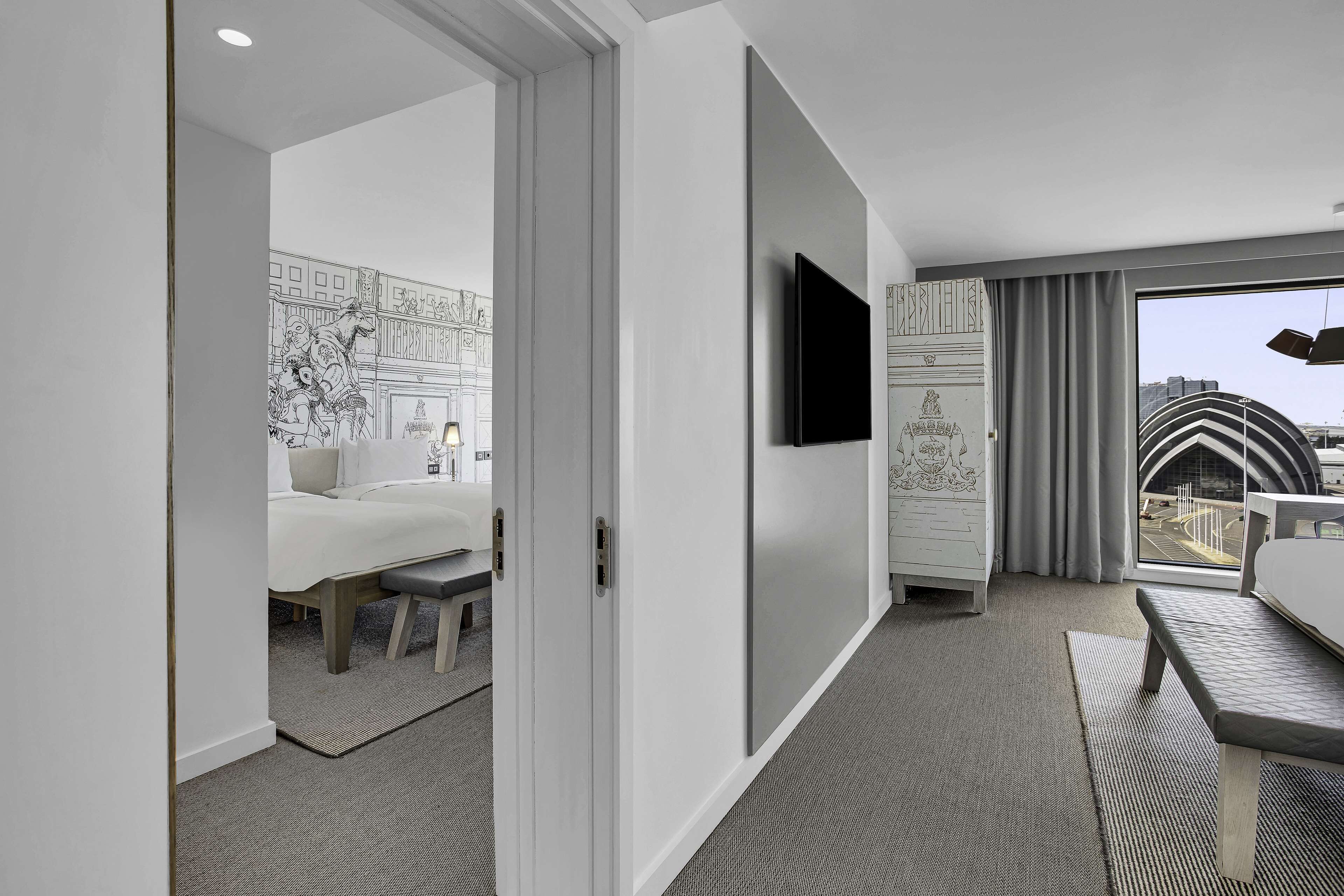Una habitación de hotel moderna con una cama, un escritorio, un televisor de pantalla plana y un amplio ventanal con vistas a la ciudad.
