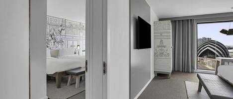 Una habitación de hotel moderna con una cama, un escritorio, un televisor de pantalla plana y un amplio ventanal con vistas a la ciudad.