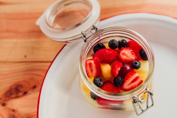A glass jar with a metal clasp lid containing sliced strawberries, blueberries, and mango pieces on a white plate with a red rim. - Radisson RED Glasgow (Glasgow)