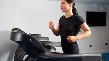 A person using a treadmill in a room with a flat-screen TV on the wall and exercise equipment on the floor.