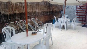 An outdoor seating area with round tables and white plastic chairs, surrounded by thatched umbrellas. - Silver Shade (Gulhi)
