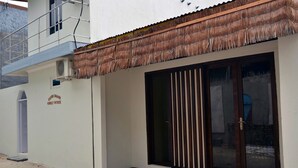 A building with a thatched roof, a large sliding glass door with vertical blinds, and a sign indicating it is a guest house. - Silver Shade (Gulhi)