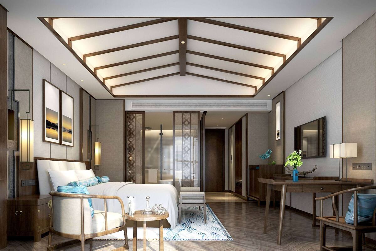 A modern hotel room with a large bed, a sitting area with a small table, and a dining area with a wooden table and chairs.