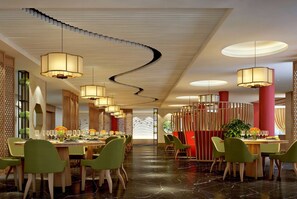 A modern dining area with green chairs, round tables, and pendant lighting. - Wyndham Guilin Pingle (Guilin)