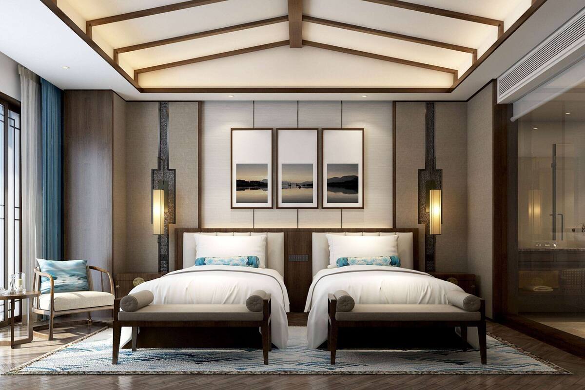 A modern hotel room with a large bed, two bedside tables, a seating area with a chair, and a large window.