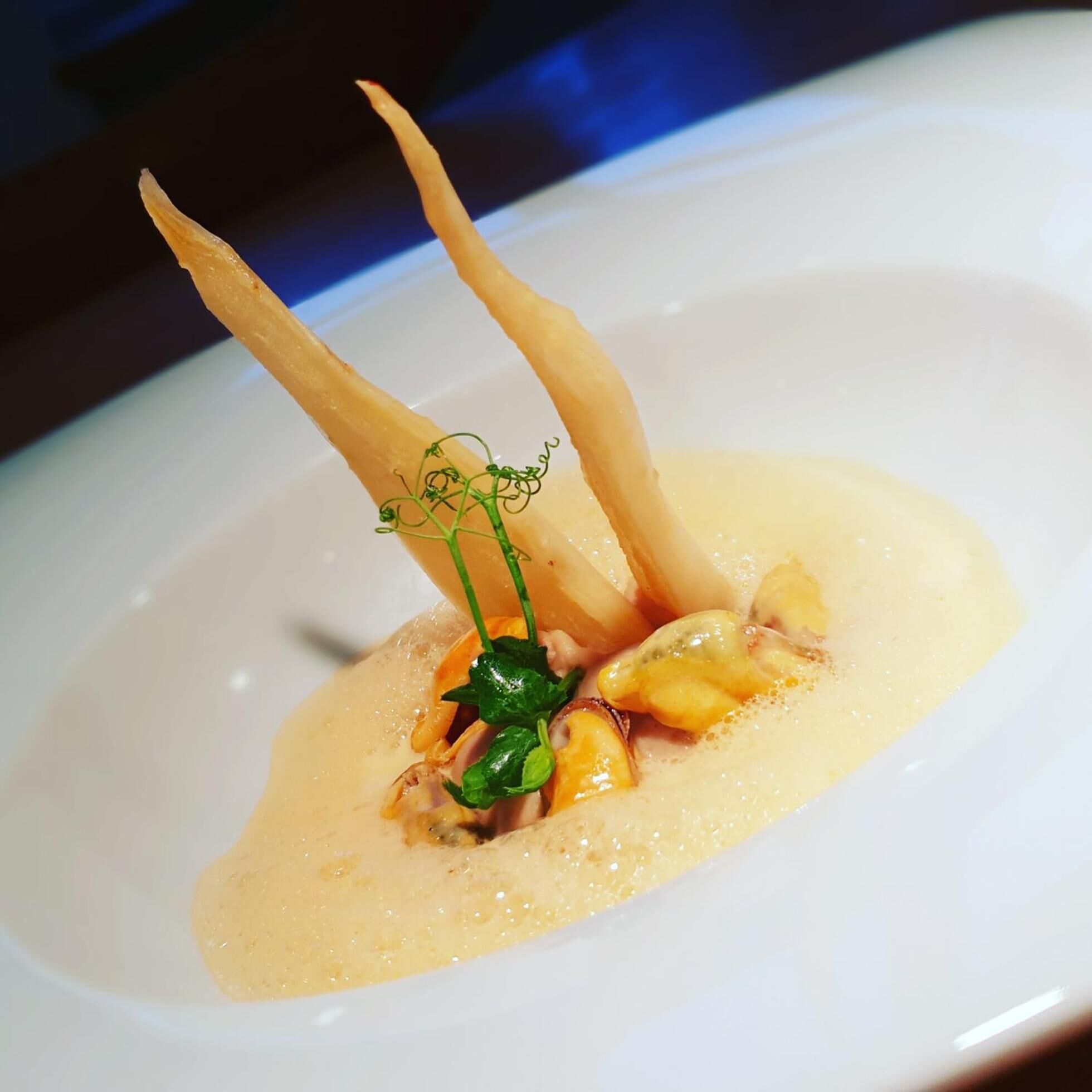 Une assiette blanche avec une sauce crémeuse, deux éléments fins et incurvés, et une petite garniture verte.
