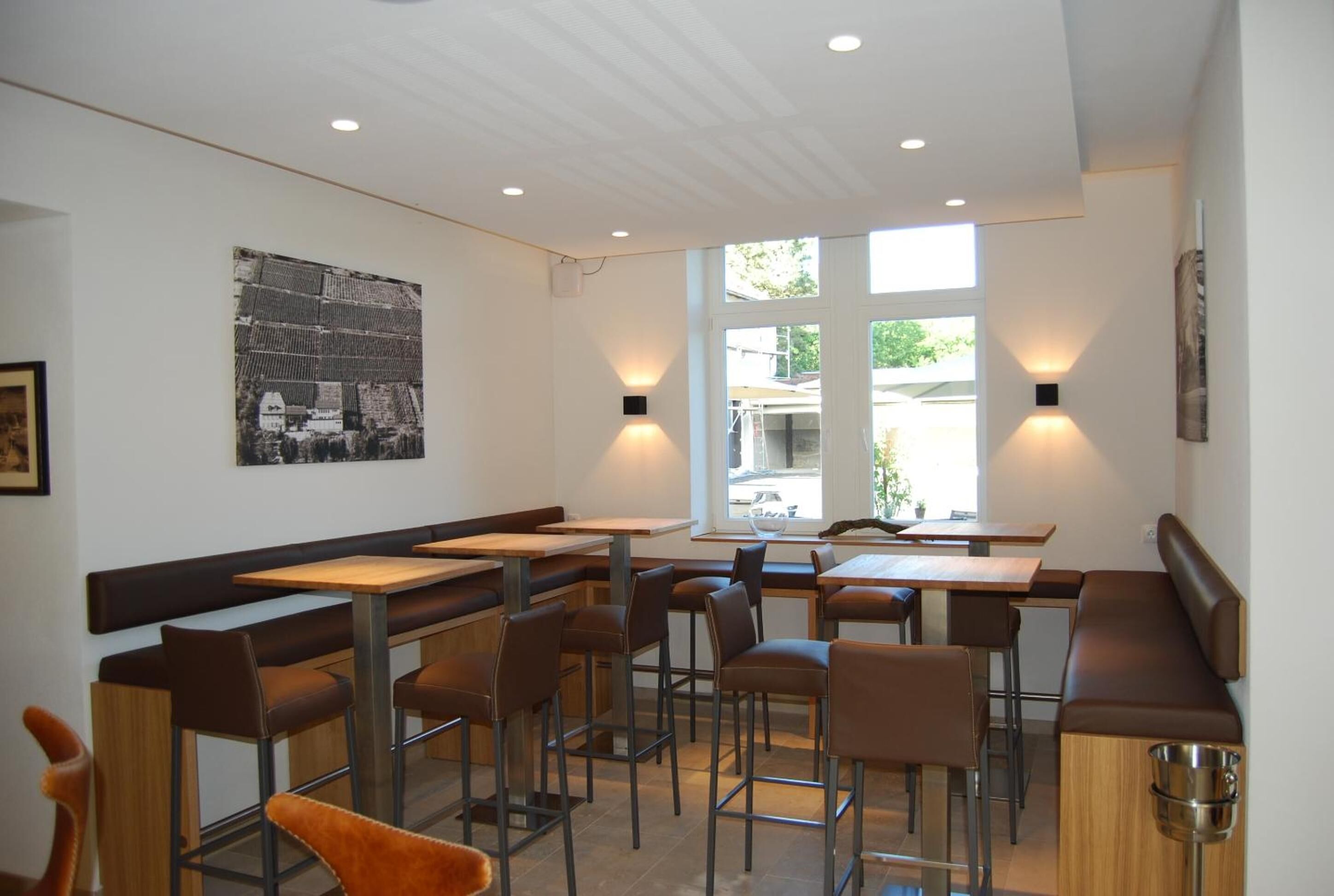 Un restaurante moderno con asientos tipo cabina, iluminación colgante y un amplio ventanal que proporciona luz natural.