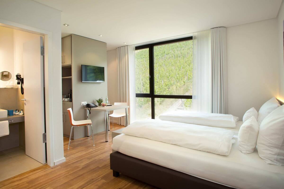 A modern hotel room with a large bed, a desk, and a TV.