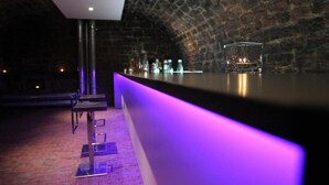 A bar area with a long counter, a stool, and a brick wall in the background. - Rebgut - Die Weinherberge (Lauda)