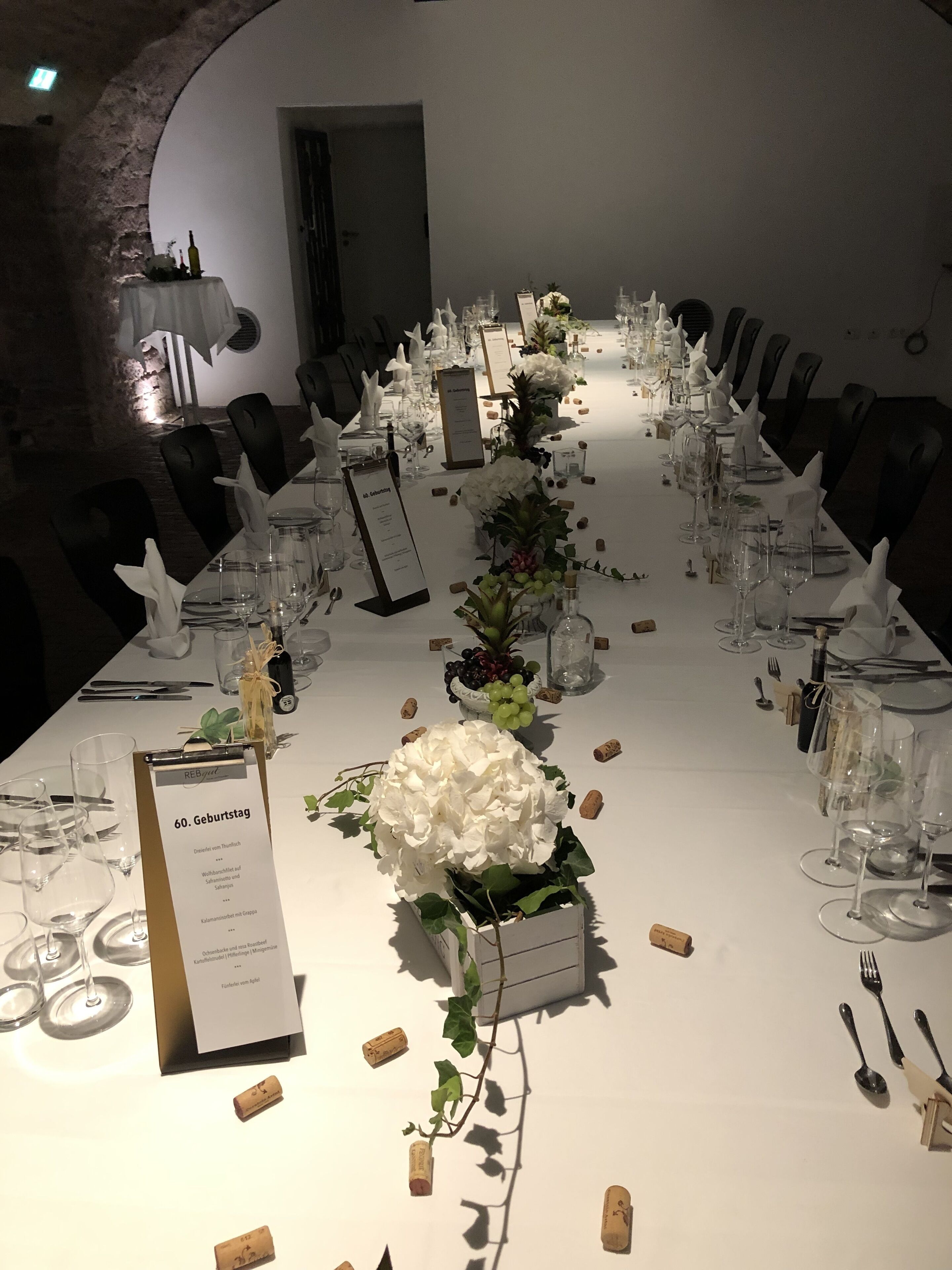A long dining table set for a formal event with white tablecloths, wine glasses, and a menu sign.