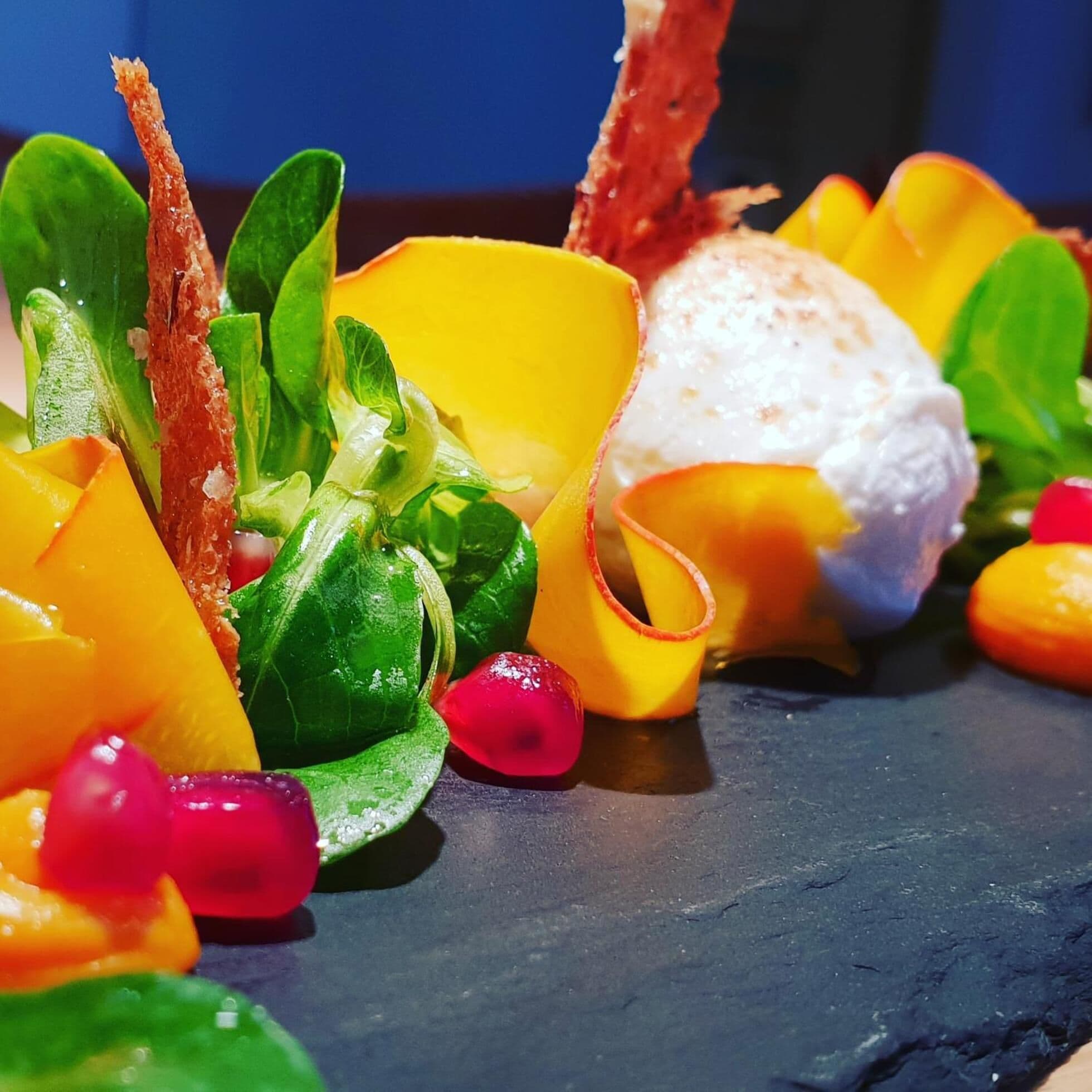 Uma tábua colorida de frutas e queijos, com diversas frutas e um queijo branco, sobre um prato de ardósia.