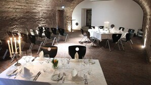 A restaurant with brick walls, white tables, and black chairs. - Rebgut - Die Weinherberge (Lauda)
