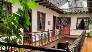A spacious interior with a high ceiling, a wooden staircase, and a balcony with a wrought iron railing. - La Posada Cuencana (Cuenca)