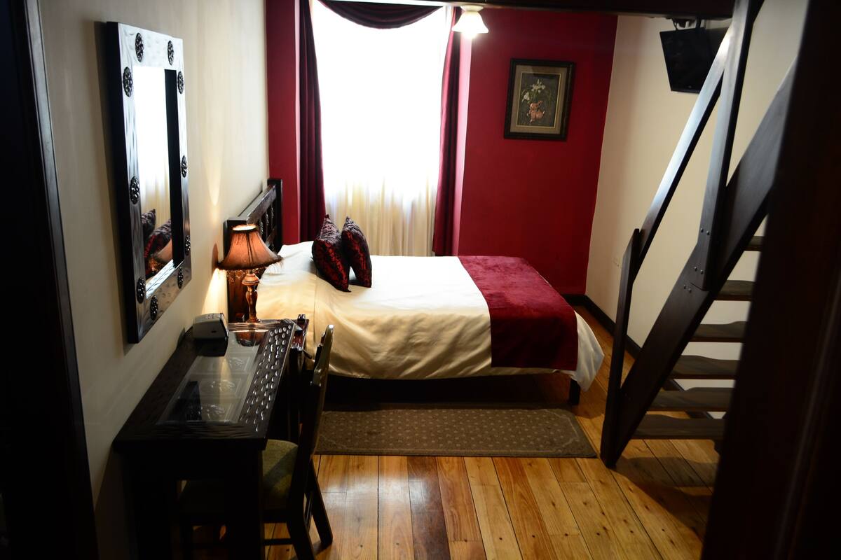 Un dormitorio con cama, escritorio, silla, lámpara y una escalera.