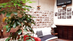 A cozy room with a red sofa, a large potted plant, a television mounted on the wall, and a patterned rug. - La Posada Cuencana (Cuenca)