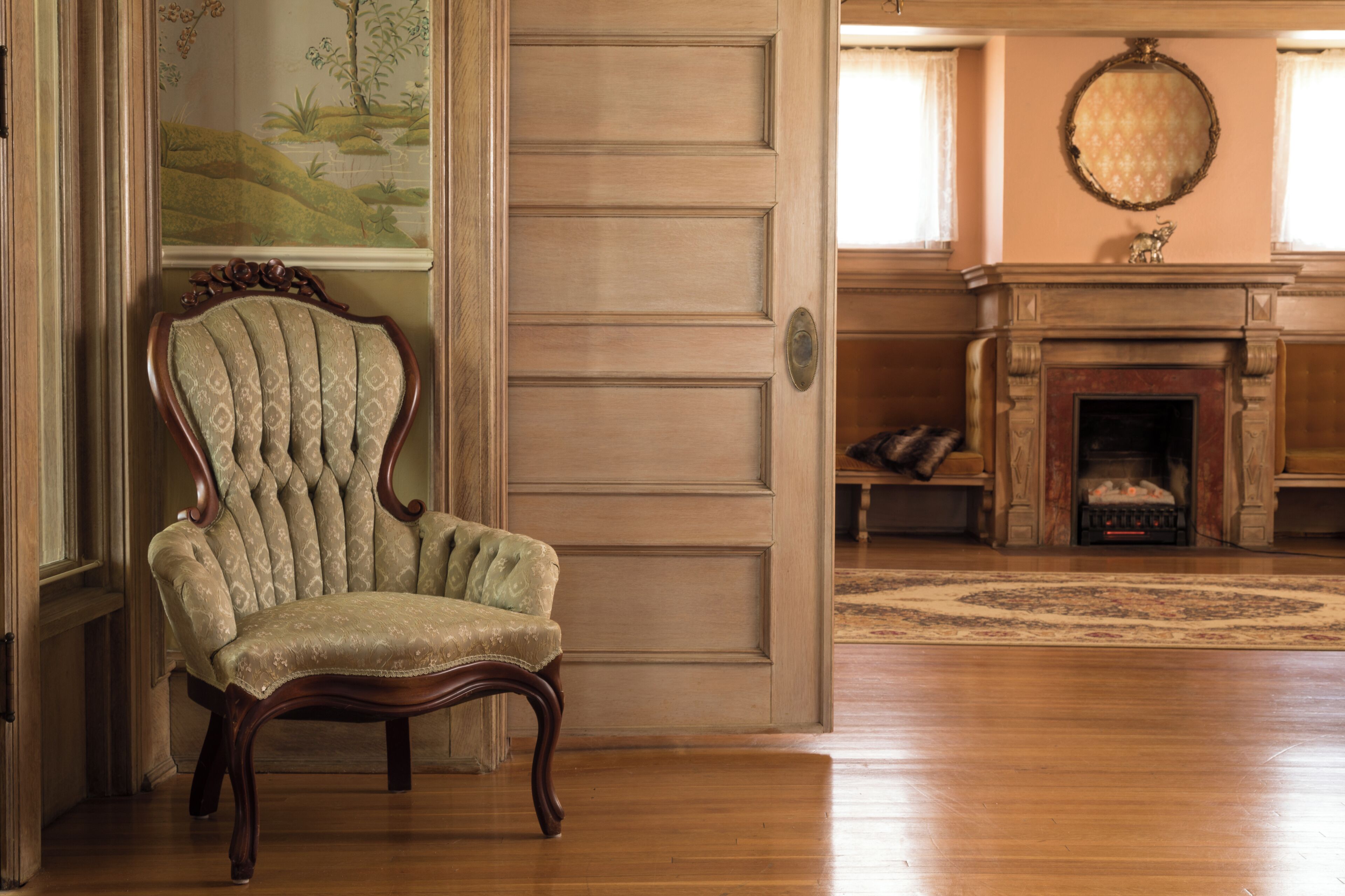 A wooden chair in a room with a fireplace, a rug, and a painting on the wall.