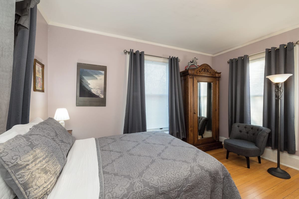 Ein Schlafzimmer mit einem Bett, einem Sessel, einem Spiegel und einer Lampe.