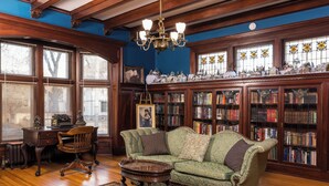 Uma biblioteca com estantes de madeira, um sofá verde, uma escrivaninha de madeira e um candelabro.