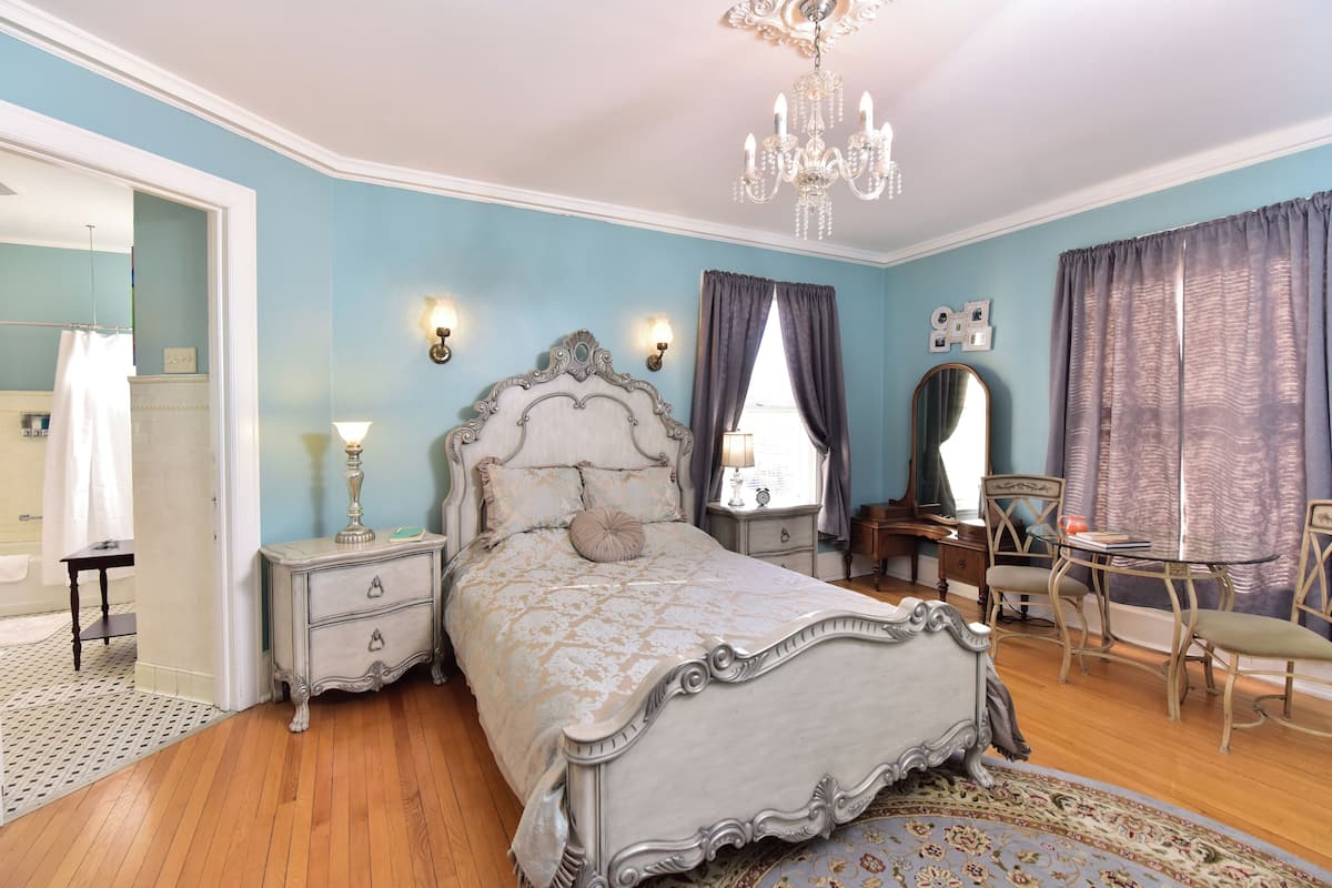 Ein Schlafzimmer mit einem großen Bett, einer Kristallleuchtre, einem Schminktisch mit Spiegel und einem Schreibtisch mit Stühlen.