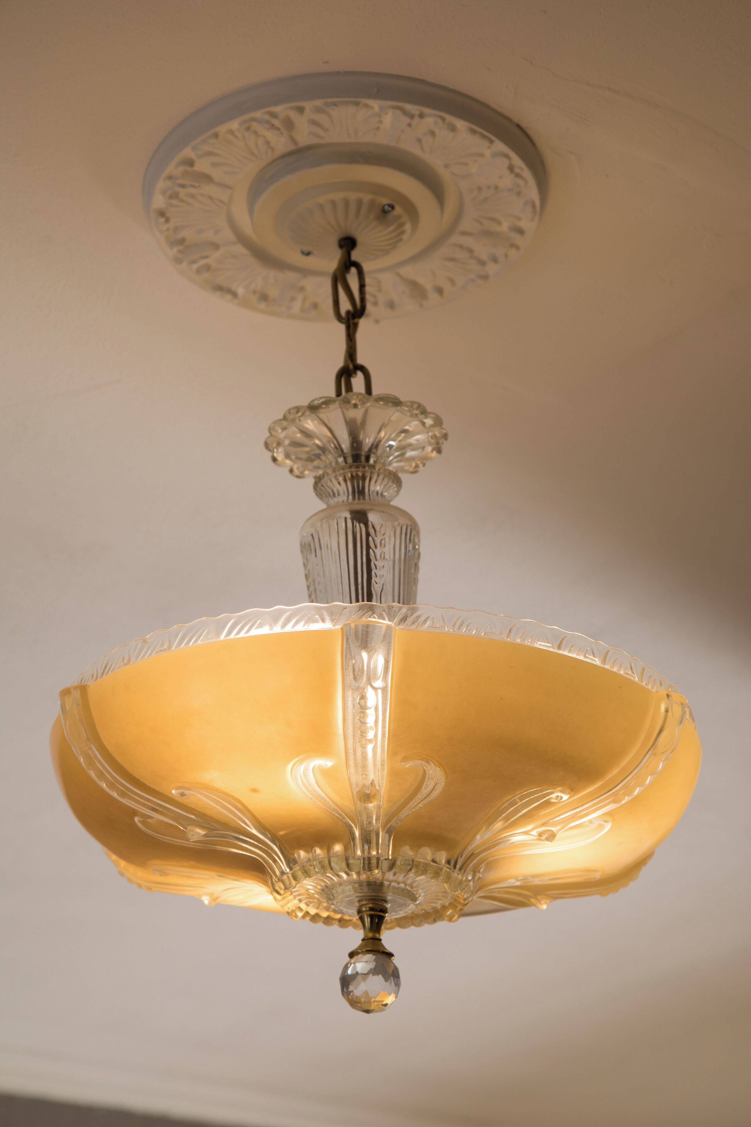 Un lampadario con paralume in vetro trasparente e una decorativa cornice a soffitto.