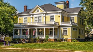 Um edifício amarelo de dois andares com uma varanda, chaminé e bandeiras americanas.